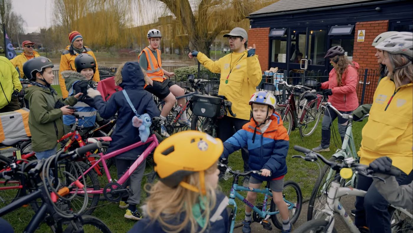 Children and adults with bikes and helmets gathered on the grass